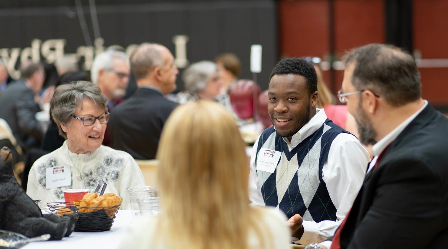 A scholarship recipient talks with scholarship donors at luncheon table